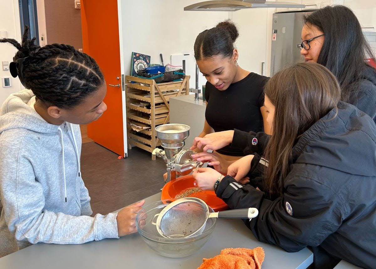 DIG students grinding corn in the Saphier Kitchen. The corn was grown in the Nettie Coit Teaching Garden